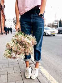 Low section of woman with bouquet standing on sidewalk