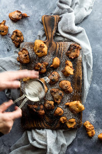 Blurry hands to depict motion of sprinkling powdered sugar on homemade fritters.