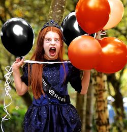 Girl shouting while holding balloons in garden