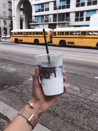 Midsection of person holding coffee cup on road in city