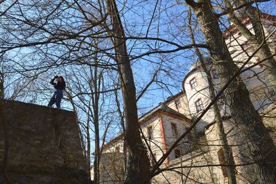Low angle view of man standing by bare tree against building