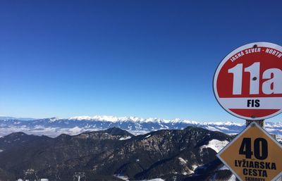 Road sign on snowcapped mountain against blue sky