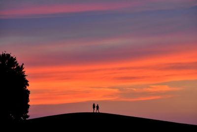 Silhouette people standing on land against sky during sunset