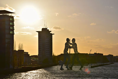 Silhouette people standing against cloudy sky at sunset
