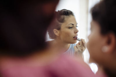 Woman applying lipstick while spending time with girlfriends at home