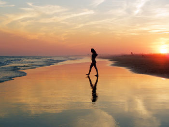 Silhouette woman standing at beach against sky during sunset