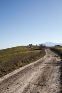 Dirt road amidst field against clear sky