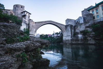 Arch bridge over river amidst buildings against sky