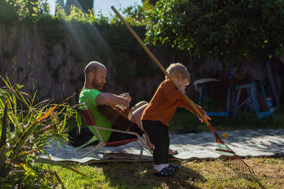 Man playing guitar while looking at son cleaning yard