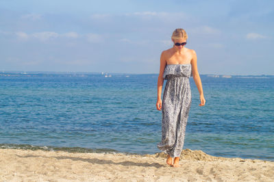 Full length of young woman standing at beach against sky