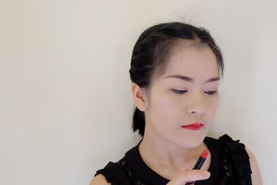 Close-up of young woman holding red lipstick against wall