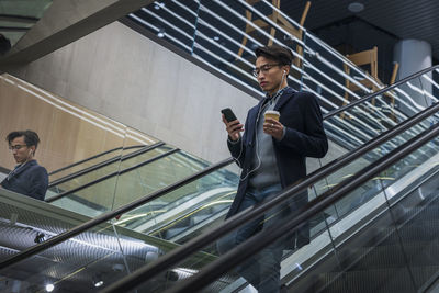 Handsome man with smartphone and paper cup on escalator