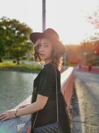 Portrait of young woman standing by lake against sky