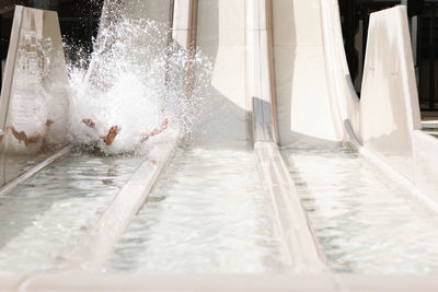 Anonymous little boy riding on water slide while spending sunny summer day in aqua park