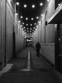 Rear view of man walking on illuminated corridor