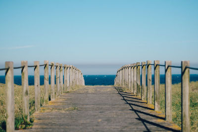 Empty boardwalk leading to sea against clear sky