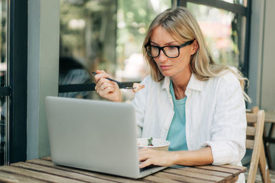 A woman has breakfast in a cafe and works remotely using a laptop.