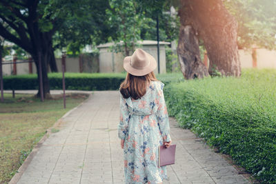 Rear view of woman walking on footpath amidst plants