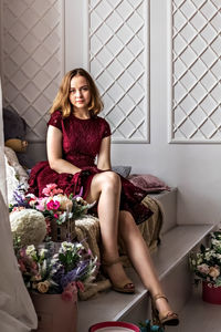 A cute stylish young girl in an elegant burgundy dress sits by the window in her room. teenager. 