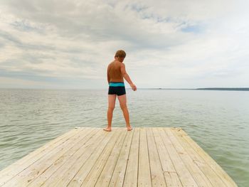 Rear view of man standing on pier over sea against sky