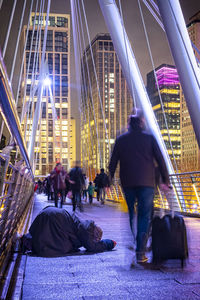 Rear view of people walking on illuminated modern buildings in city