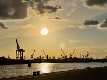 Silhouette cranes at commercial dock against sky during sunset