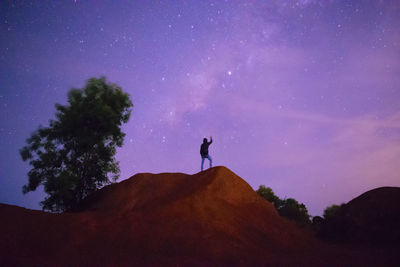 Silhouette man standing on rock against sky at night