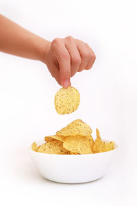 Close-up of hand holding potato chip over bowl against white background