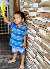 Boy playing with toy while standing against wall