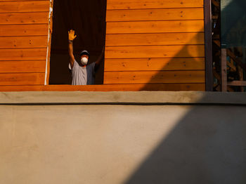 Full length of man sitting on wood against wall