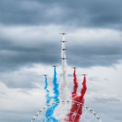 Low angle view of ferries wheel against airshow in cloudy sky