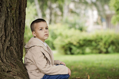 Portrait of cute boy standing against tree trunk