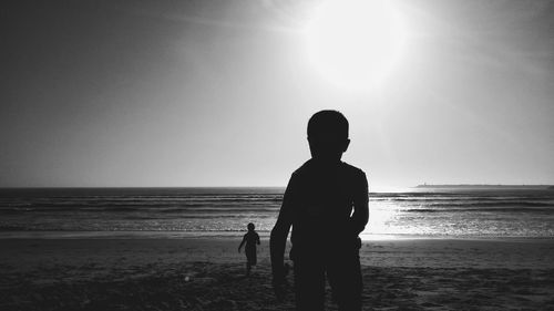 Rear view of silhouette boy standing on beach against clear sky