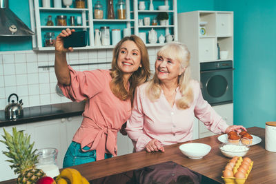 Cheerful mother and daughter doing selfie at kitchen