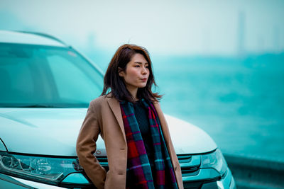 Beautiful young woman standing by car against sky