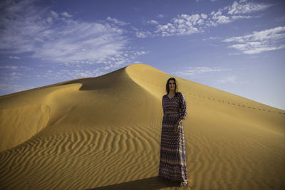 Woman standing on sand dune in desert against sky