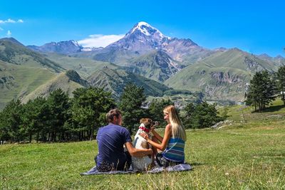 Side view of woman sitting on field against mountain