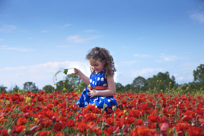 Girl playing with flowers on field against sky