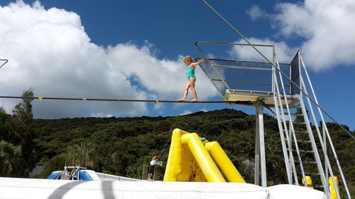 Low angle view of girl walking on tightrope against sky