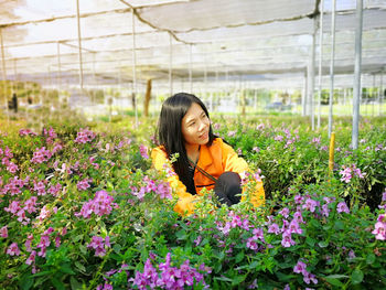 Woman standing by flower plants in greenhouse