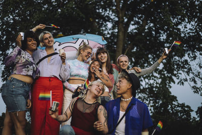 Happy friends enjoying during lgbtqia rights parade against tree