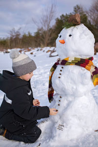 Boy in hat makes snowman, which was the nose of snowman, smiling. winter family weekend, lifestyle