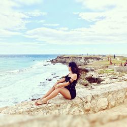 Side view of woman sitting on retaining wall at beach in isla mujeres