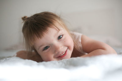 Happy funny girl toddler lifestyle with a smile lying on the bed, close-up, concept happy childhood,