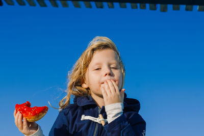 Girl in delight eats donut with red icing, food stained her mouth