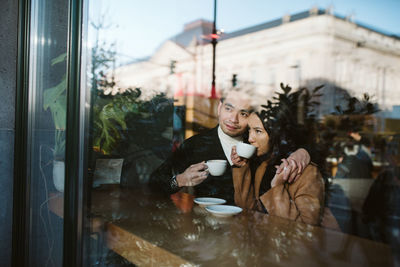 Young woman using phone while looking through window