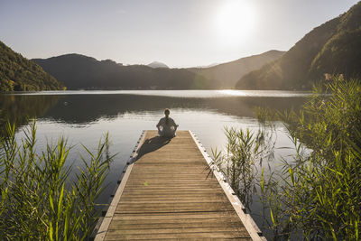 Mature woman meditating on jetty over lake by mountain range
