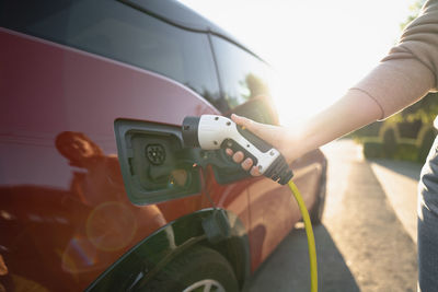 Hand of woman plugging charger in electric car at vehicle charging station