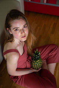 Portrait of young woman with pineapple sitting at home