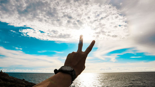 Hand by sea against sky
